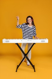 Smiling woman in headphones playing synthesizer on orange background