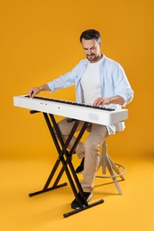 Photo of Bearded man playing synthesizer on orange background