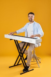 Photo of Smiling man playing synthesizer on orange background