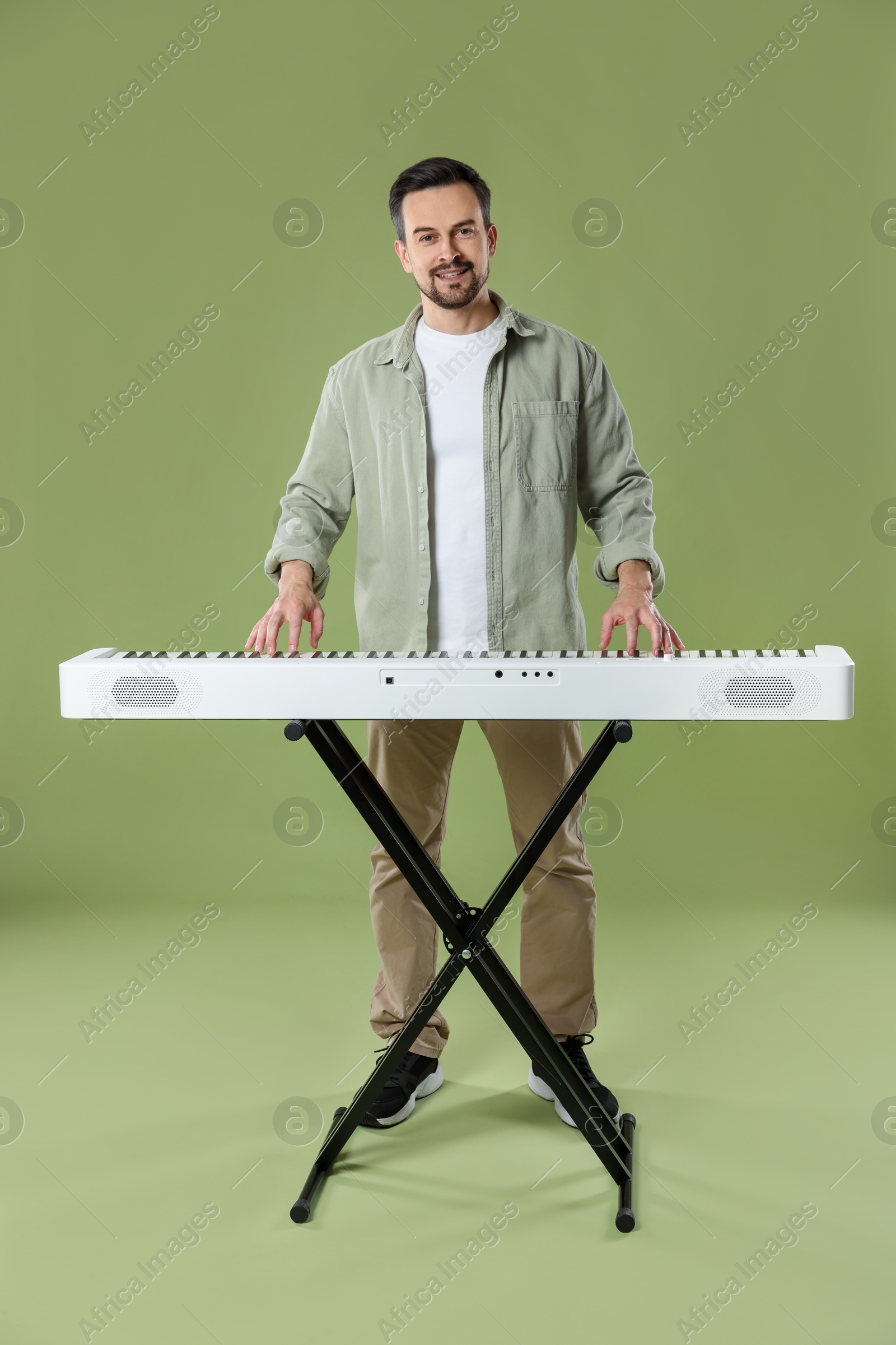 Photo of Smiling man playing synthesizer on olive background