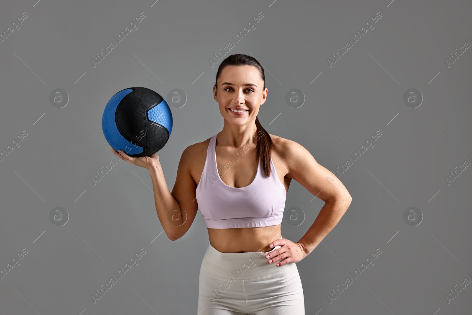 Photo of Woman in gym clothes doing exercise with medicine ball on grey background