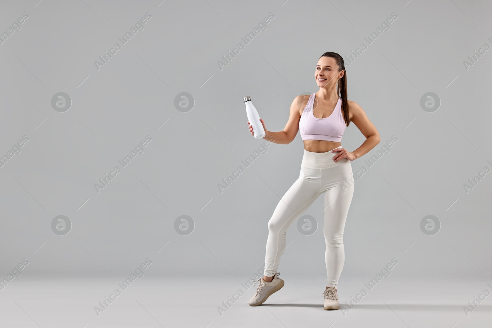 Photo of Woman in gym clothes with thermo bottle on grey background