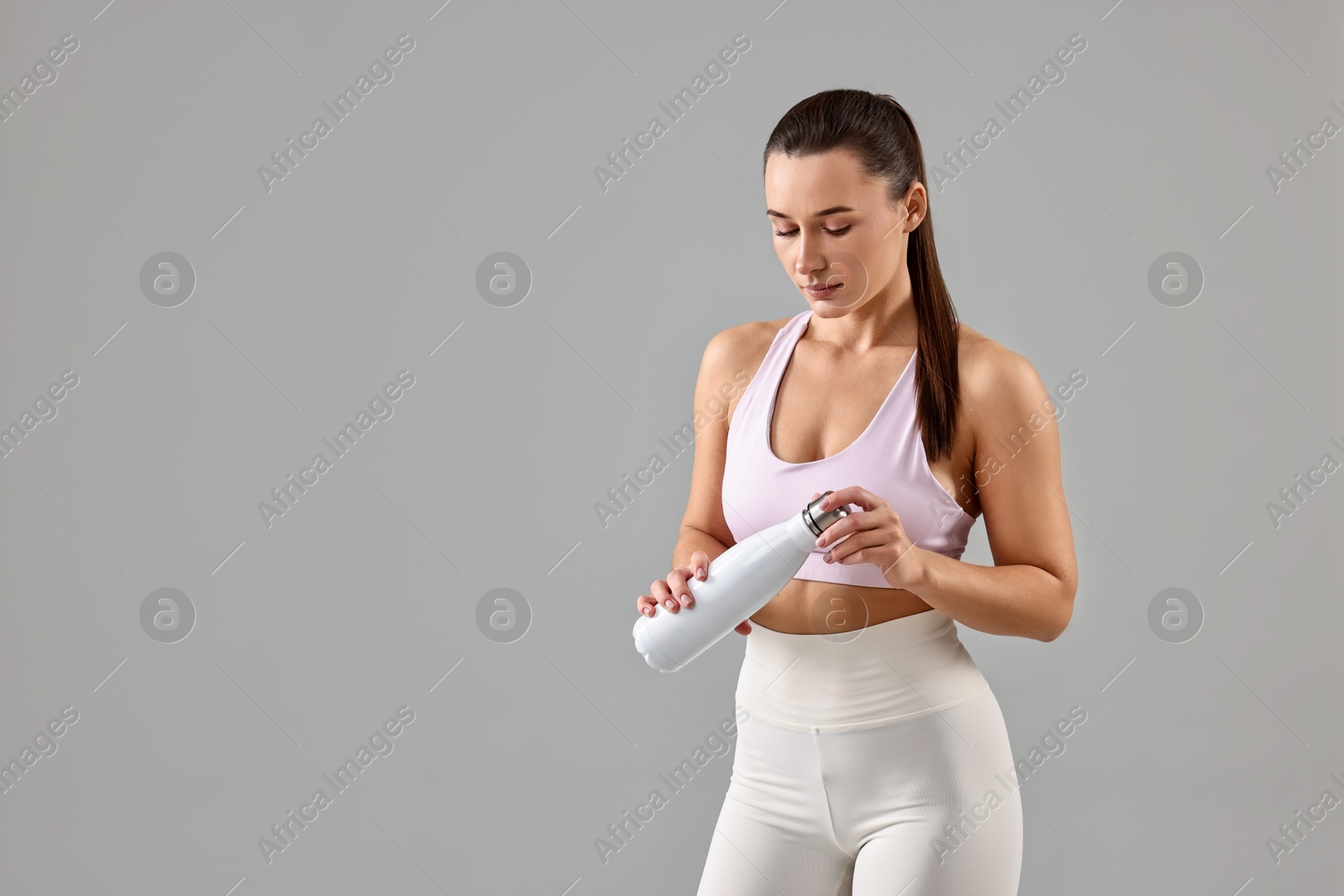 Photo of Woman in gym clothes with thermo bottle on grey background, space for text