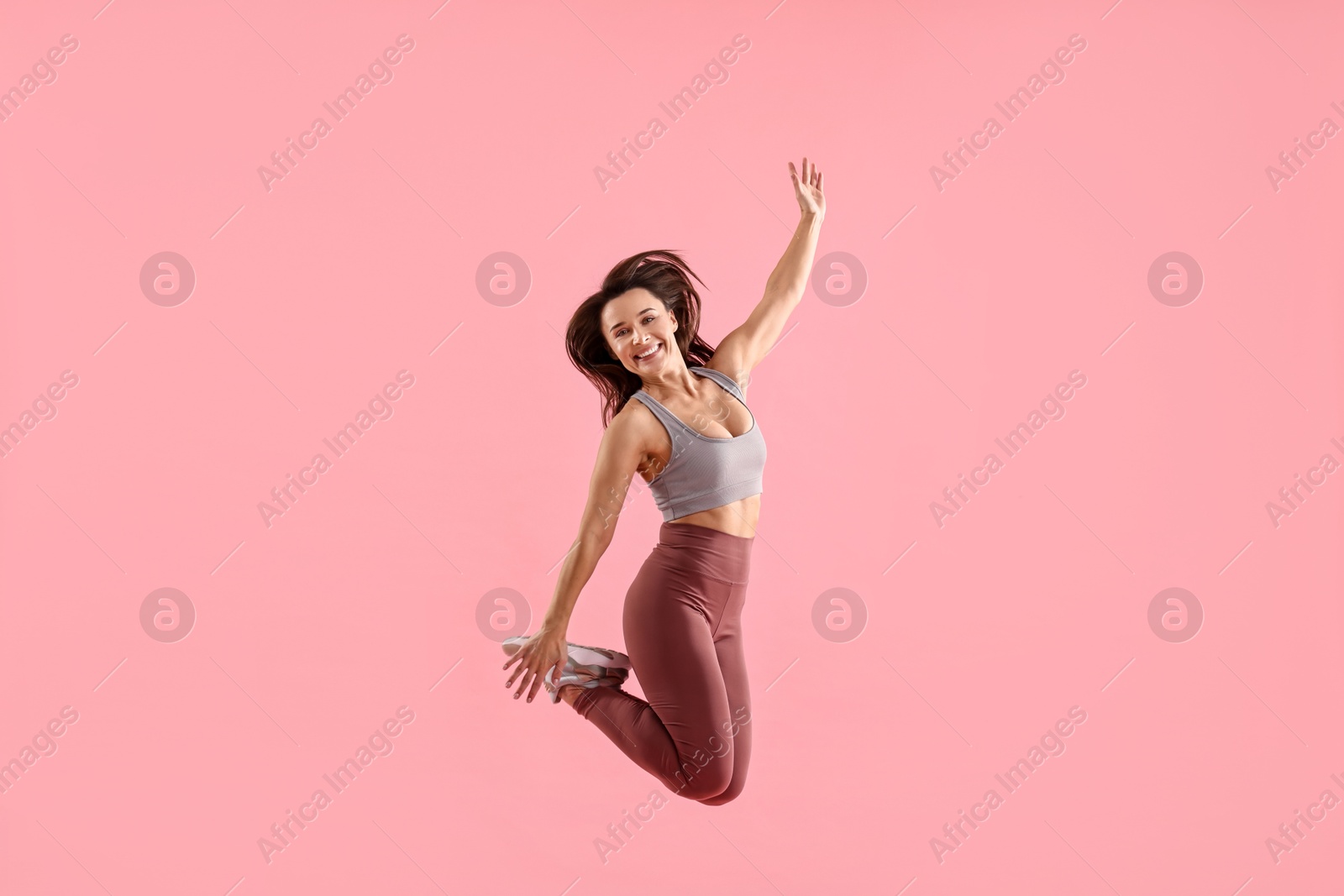 Photo of Woman in gym clothes jumping on pink background