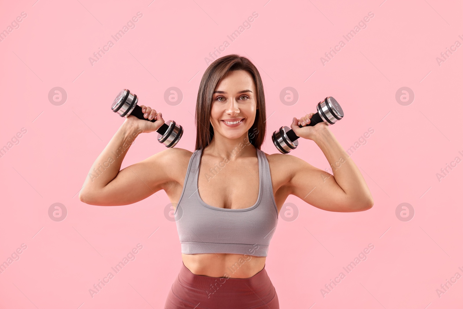 Photo of Woman in gym clothes exercising with dumbbells on pink background