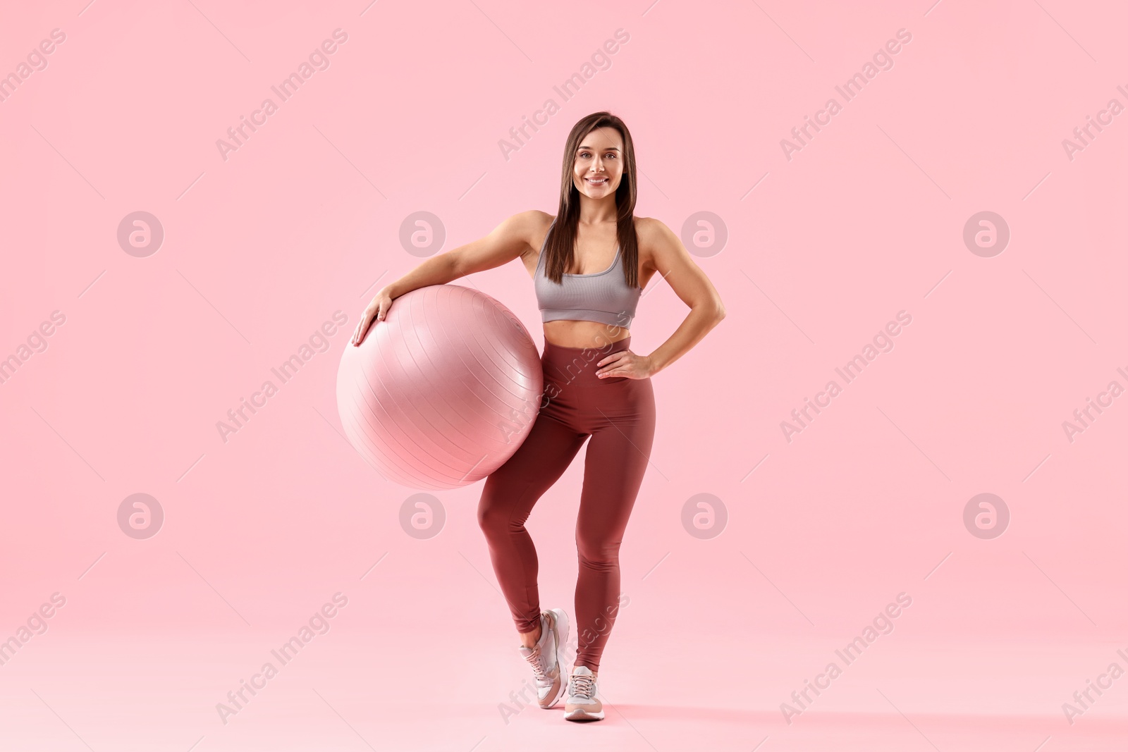 Photo of Woman in gym clothes with fitness ball on pink background