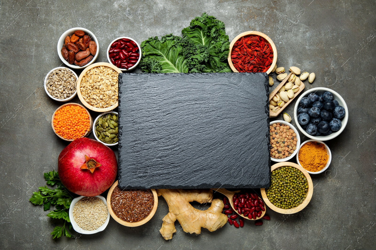 Photo of Superfood. Different healthy food products and blank board on grey table, flat lay. Space for text