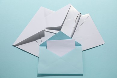 Photo of Paper envelopes with card and pen on light blue background, above view. Mockup for design