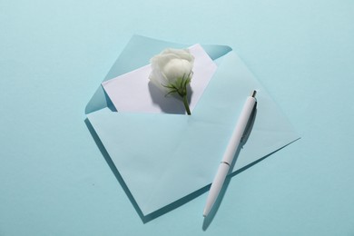 Photo of Paper envelope with letter, flower and pen on light blue background, above view. Mockup for design