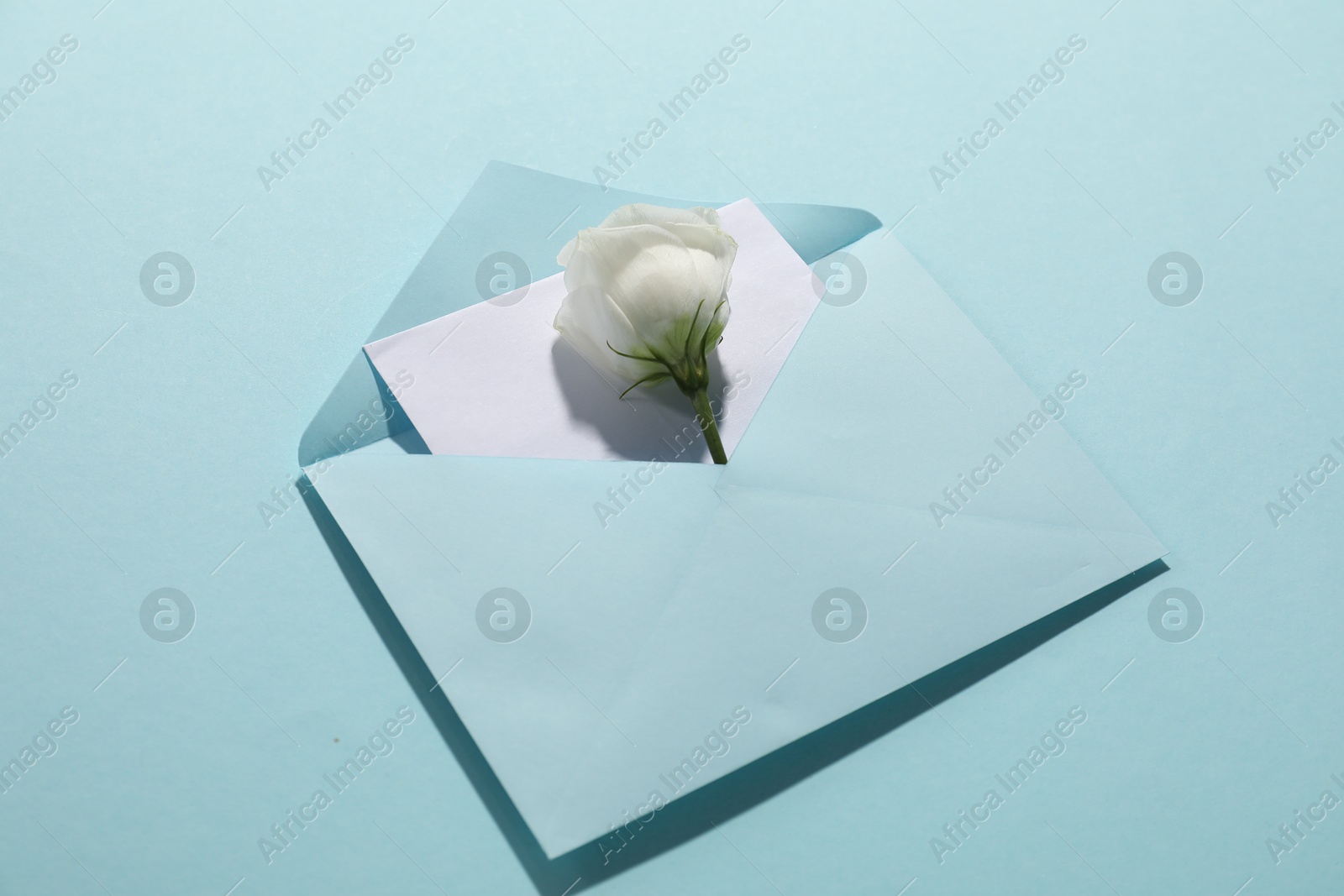 Photo of Paper envelope with letter and flower on light blue background, closeup. Mockup for design