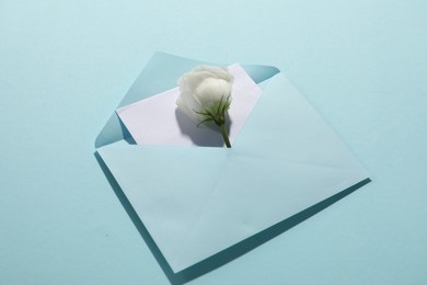 Paper envelope with letter and flower on light blue background, closeup. Mockup for design