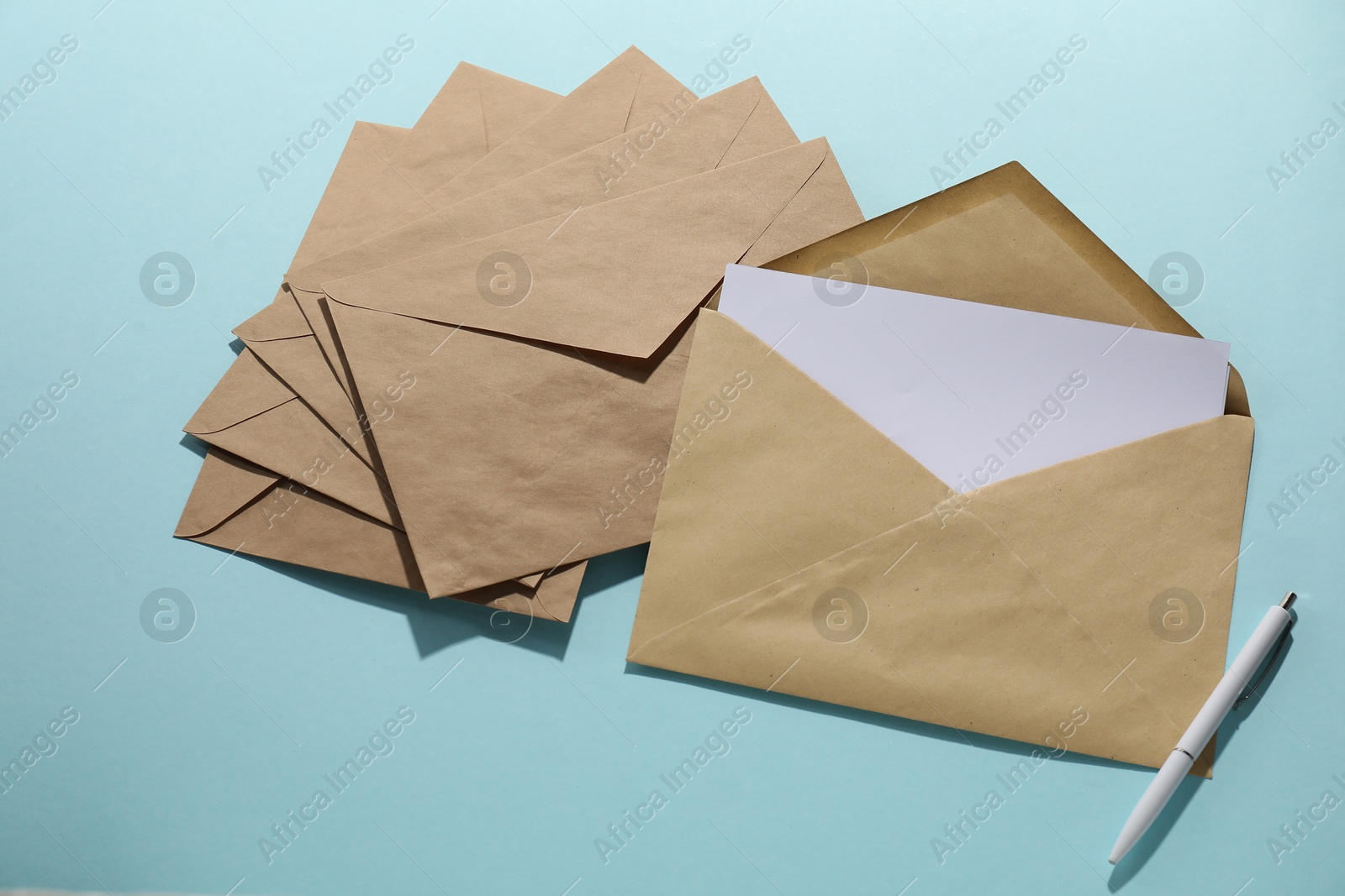 Photo of Kraft paper envelopes with letter and pen on light blue background, flat lay. Mockup for design