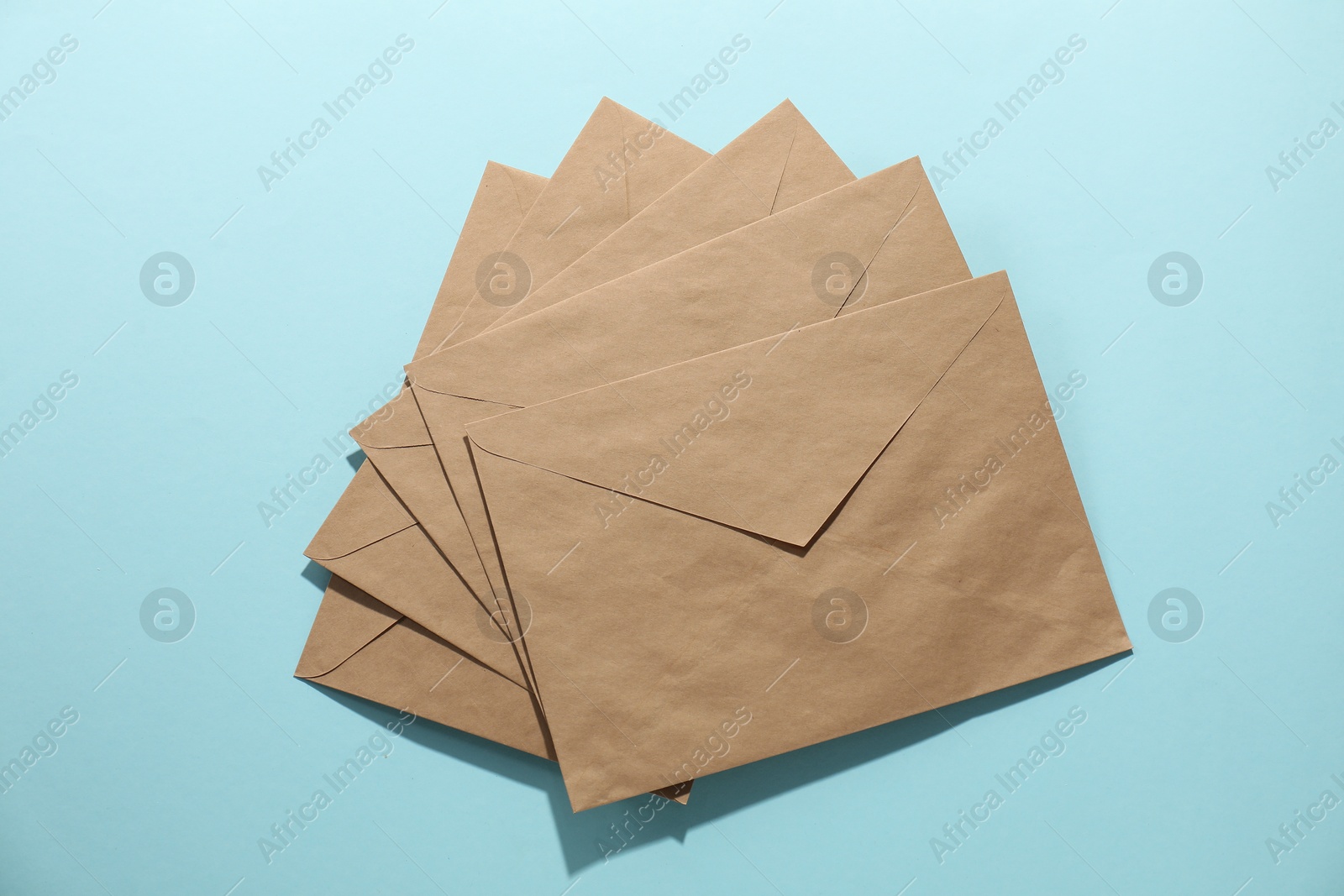 Photo of Kraft paper envelopes on light blue background, flat lay. Mockup for design