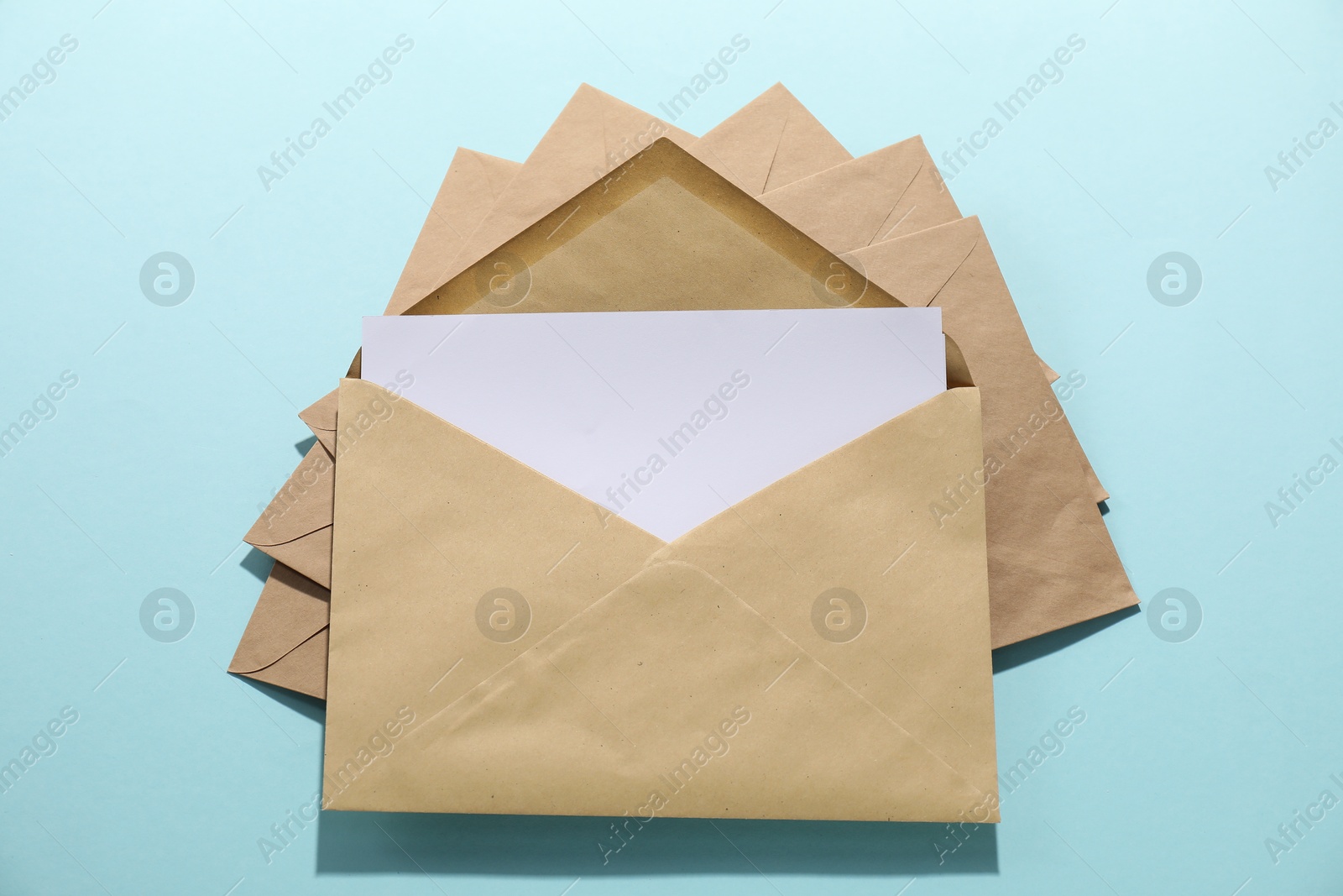 Photo of Kraft paper envelopes with letter on light blue background, top view. Mockup for design