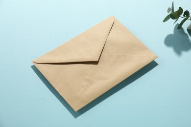 Photo of Kraft paper envelope and eucalyptus branch on light blue background. Mockup for design