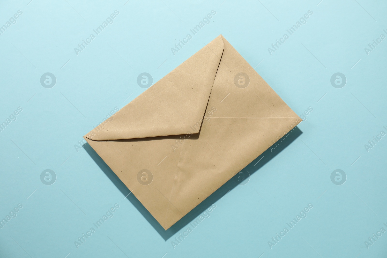 Photo of Kraft paper envelope on light blue background, top view. Mockup for design