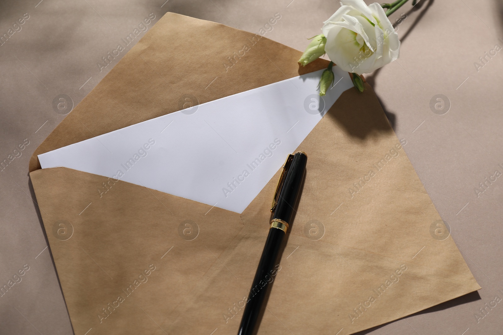 Photo of Kraft paper envelope with letter, pen and flower on dark beige background, above view. Mockup for design