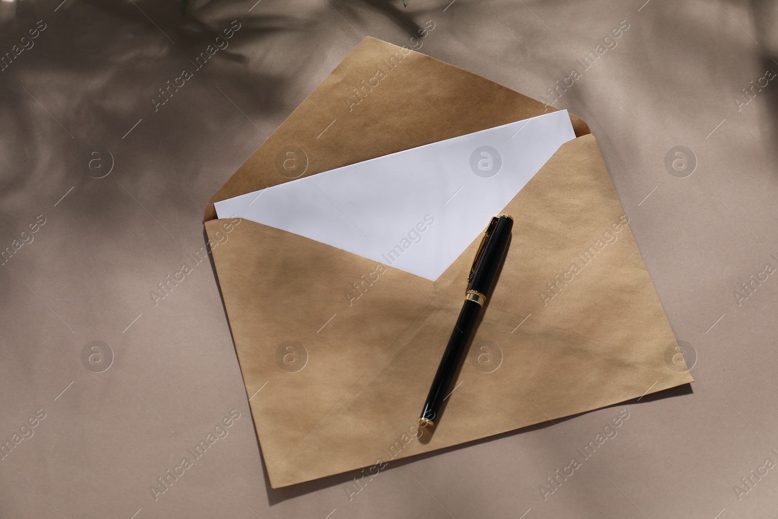 Photo of Kraft paper envelope with letter and pen on dark beige background, top view. Mockup for design