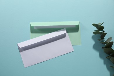 Paper envelopes and eucalyptus branch on light blue background, flat lay. Mockup for design