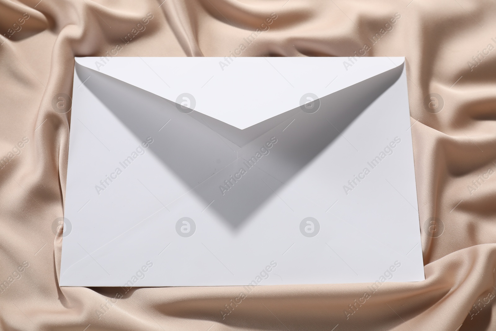 Photo of Paper envelope on beige silk fabric, top view. Mockup for design