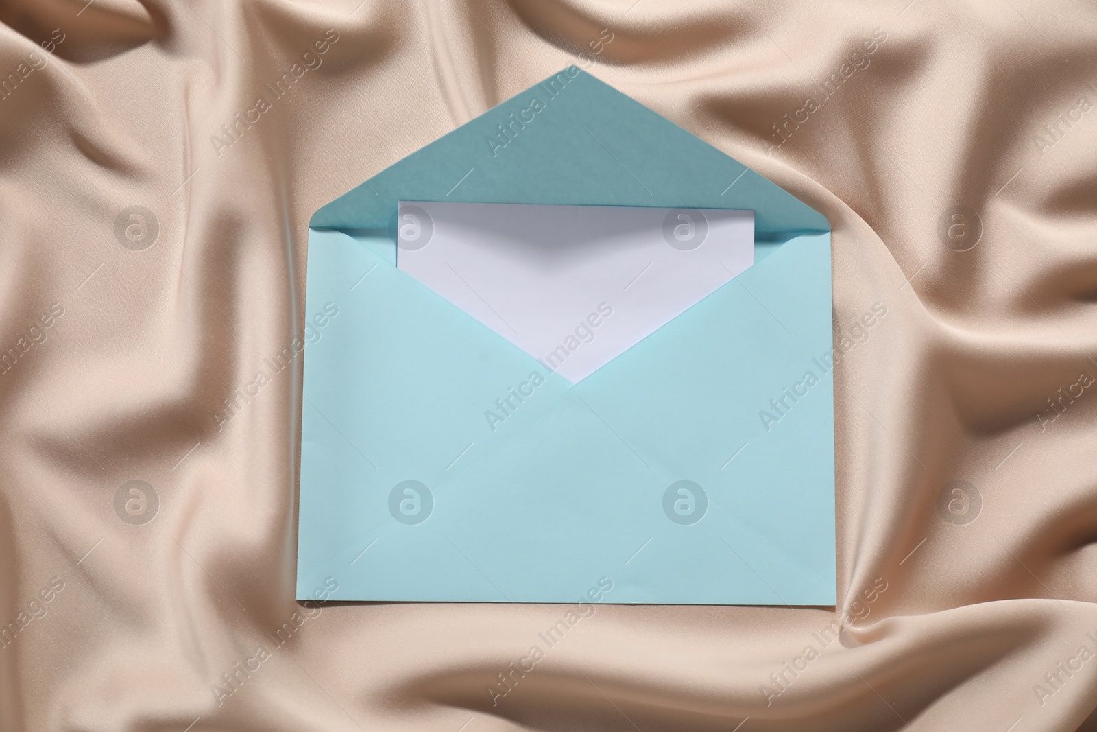 Photo of Paper envelope with letter on beige silk fabric, top view. Mockup for design