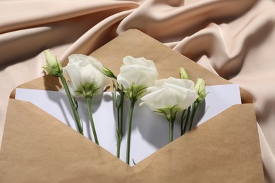 Kraft paper envelope with letter and flowers on beige silk fabric, above view