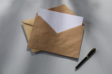 Kraft paper envelopes with letter and fountain pen on grey background, top view. Mockup for design