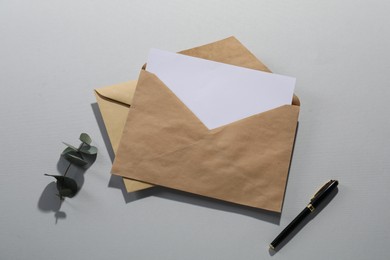 Photo of Kraft paper envelopes with letter, fountain pen and eucalyptus branch on grey background, flat lay. Mockup for design