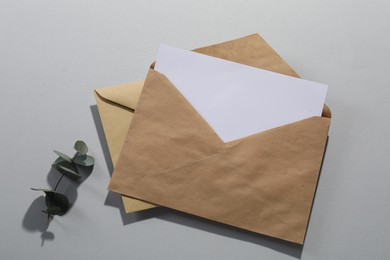 Photo of Kraft paper envelopes with letter and eucalyptus branch on grey background, top view. Mockup for design