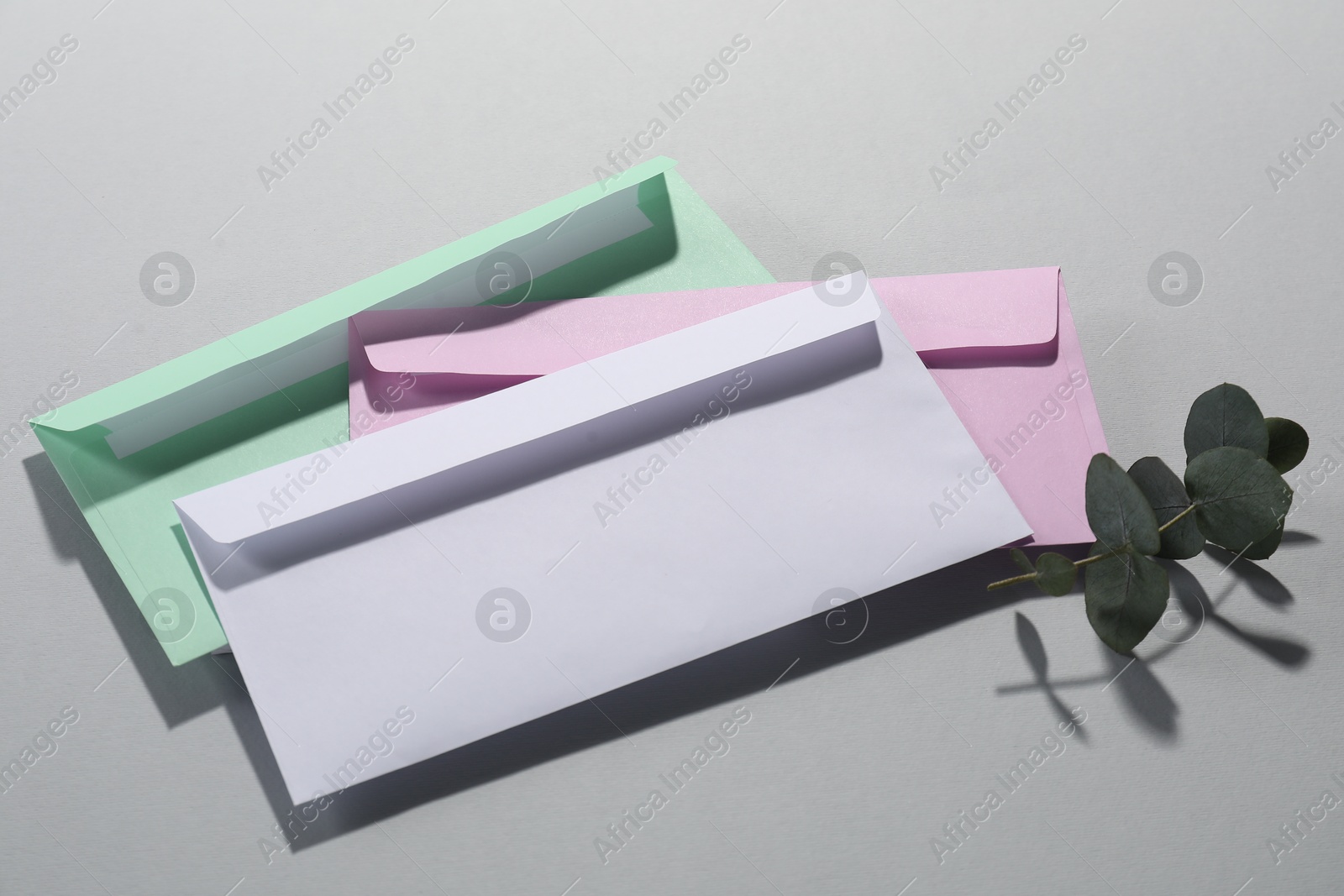 Photo of Paper envelopes and eucalyptus branch on grey background, above view. Mockup for design