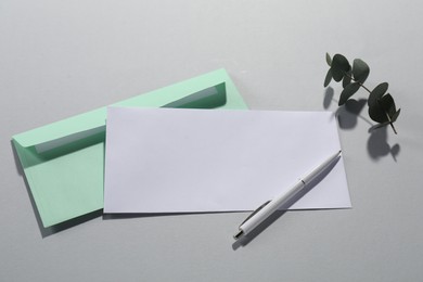 Paper envelopes, pen and eucalyptus branch on grey background, flat lay. Mockup for design