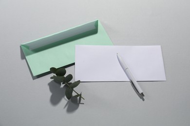 Photo of Paper envelopes, pen and eucalyptus branch on grey background, flat lay. Mockup for design