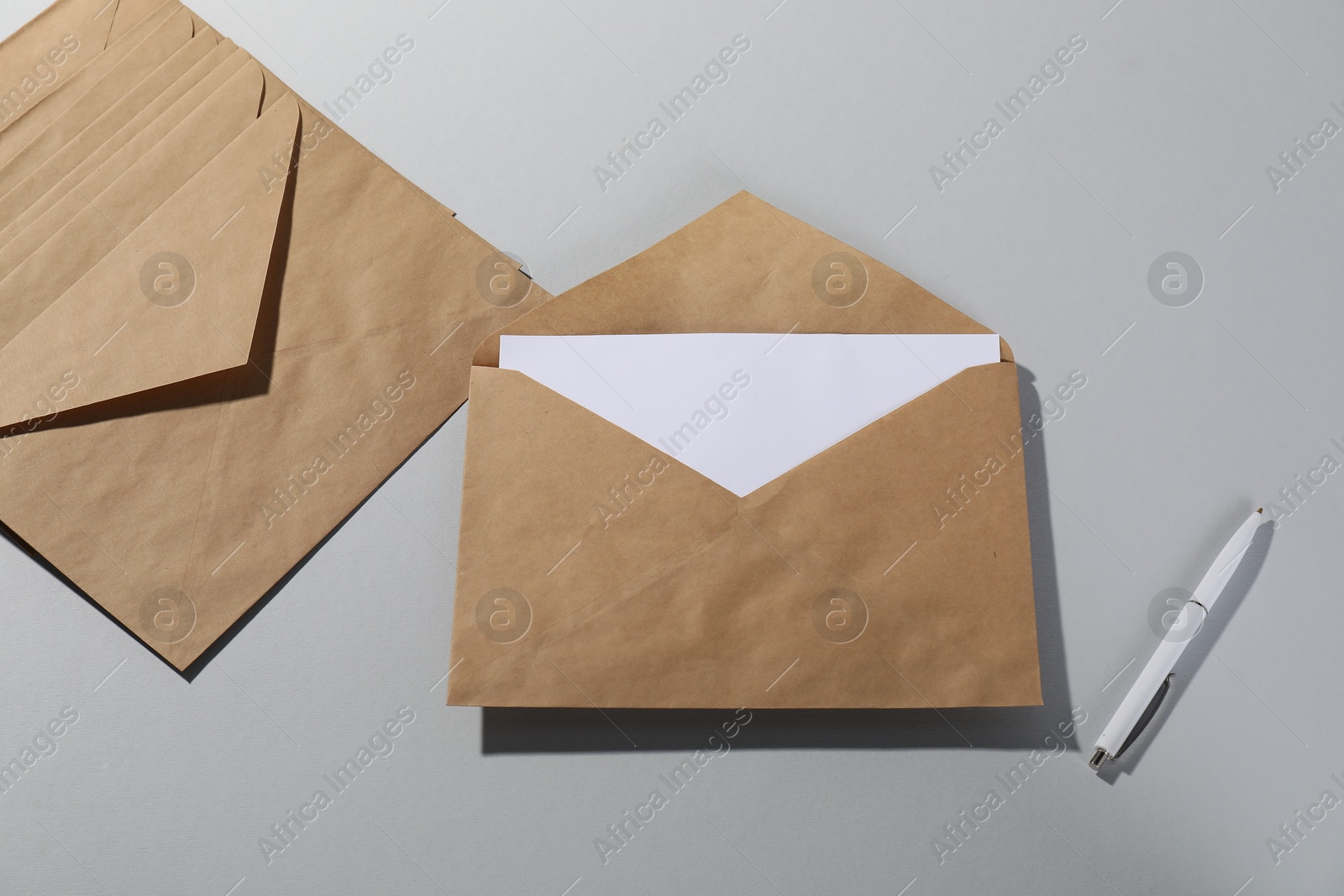 Photo of Kraft paper envelopes with letter and pen on grey background, flat lay. Mockup for design