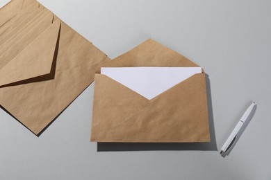 Kraft paper envelopes with letter and pen on grey background, flat lay. Mockup for design