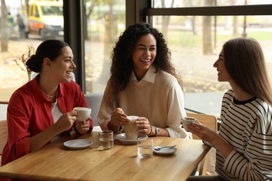 Photo of Happy women with coffee drinks chatting in cafe