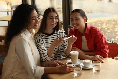 Photo of Woman taking picture of coffee drinks during meeting with her friends in cafe