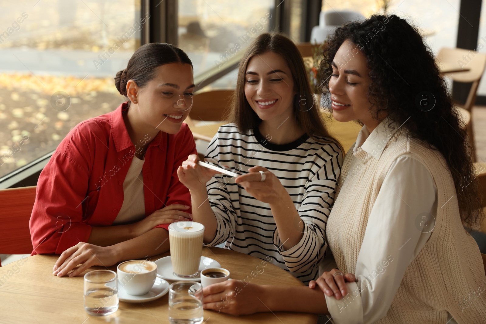 Photo of Woman taking picture of coffee drinks during meeting with her friends in cafe