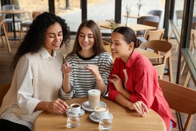 Photo of Woman taking picture of coffee drinks during meeting with her friends in cafe