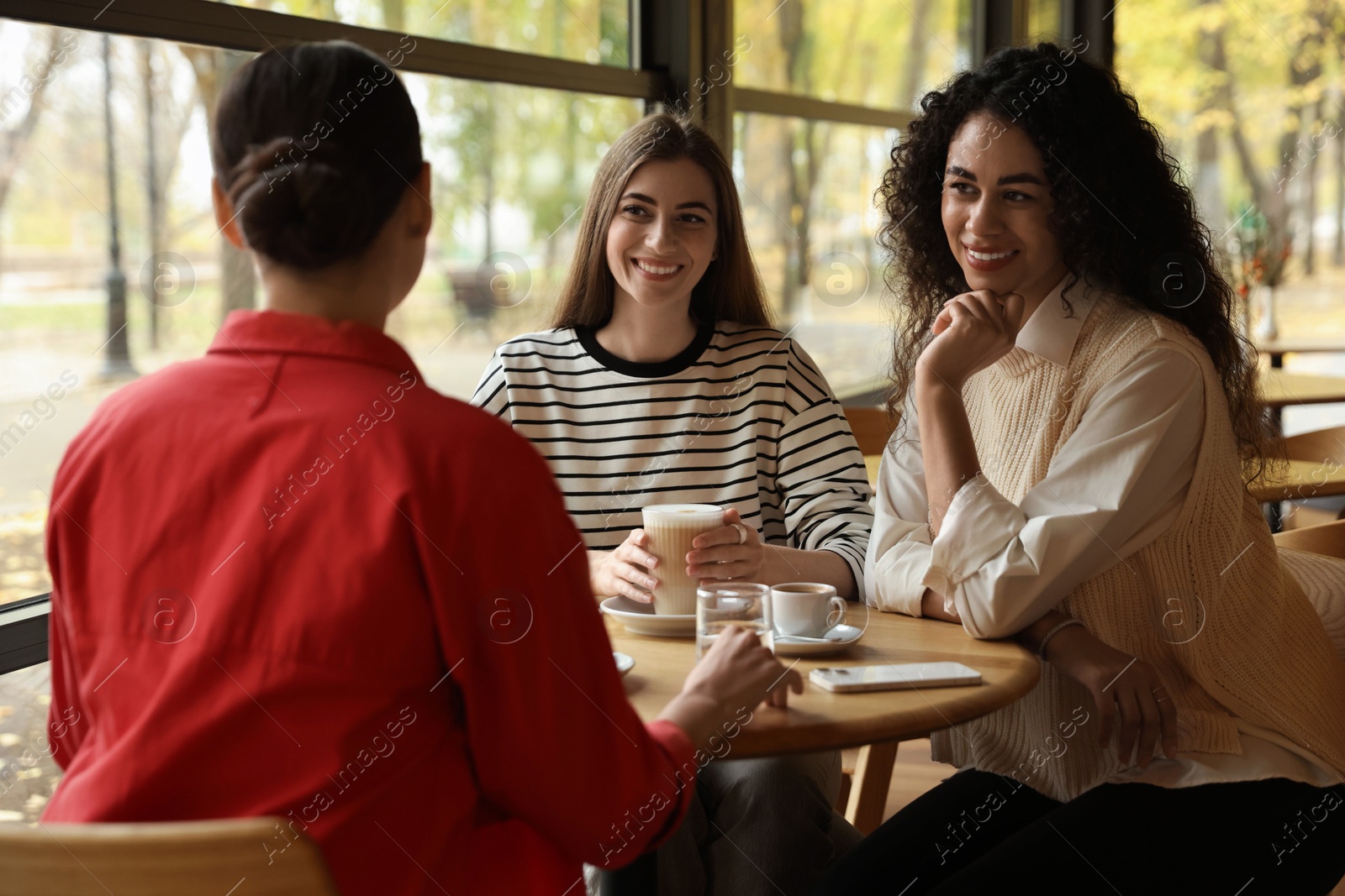 Photo of Happy women with coffee drinks chatting in cafe