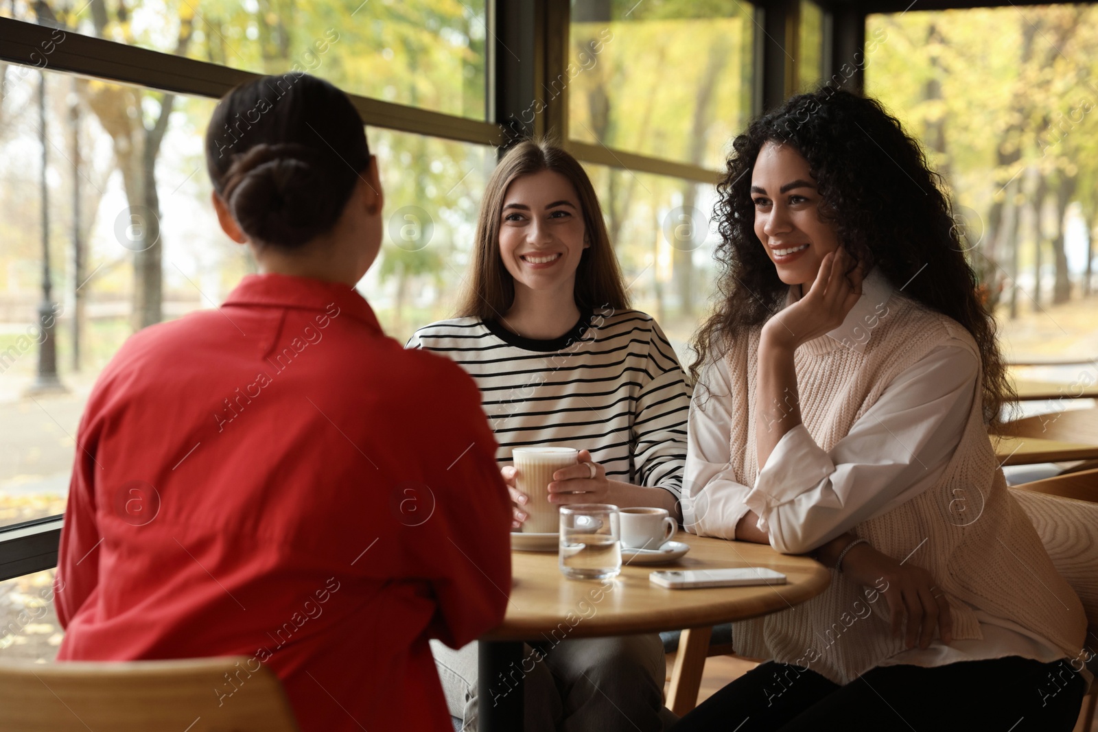 Photo of Happy women with coffee drinks chatting in cafe