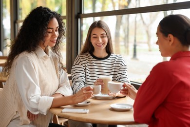 Photo of Happy women with coffee drinks chatting in cafe