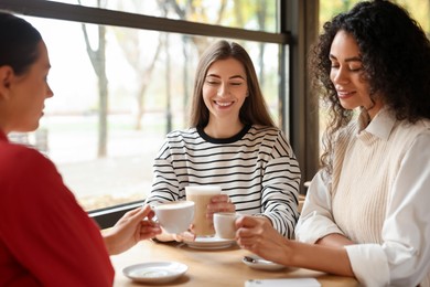 Photo of Happy women with coffee drinks chatting in cafe