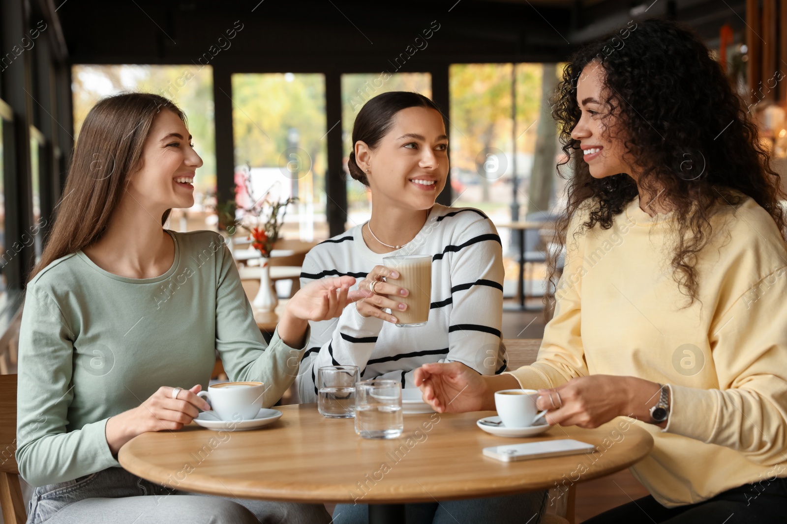 Photo of Happy women with coffee drinks chatting in cafe