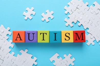 Photo of Word Autism made of colorful cubes and puzzle on light blue background, flat lay