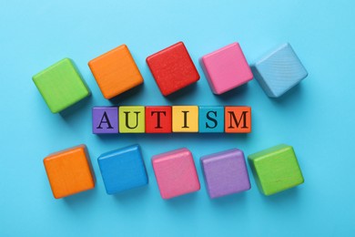 Photo of Word Autism made of colorful cubes on light blue background, top view