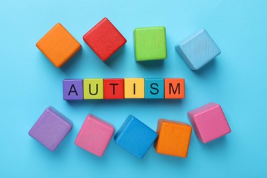 Photo of Word Autism made of colorful cubes on light blue background, top view