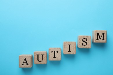 Photo of Word Autism made of wooden cubes on light blue background, top view. Space for text