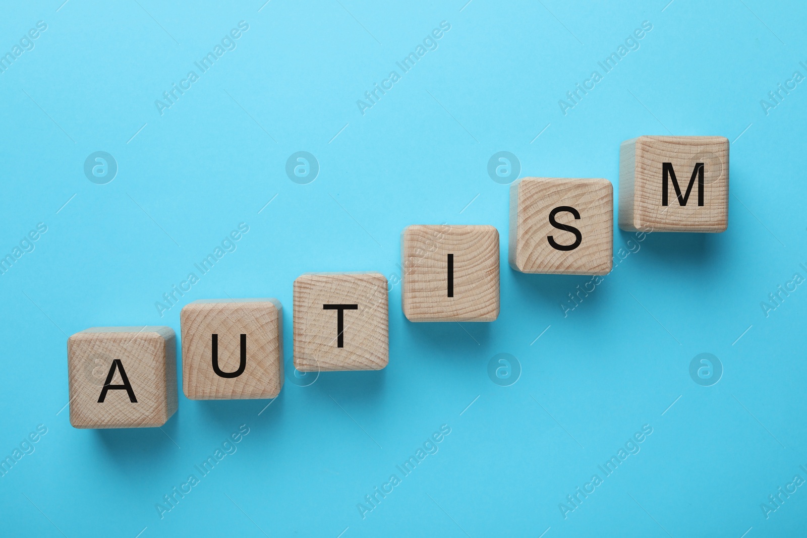 Photo of Word Autism made of wooden cubes on light blue background, top view