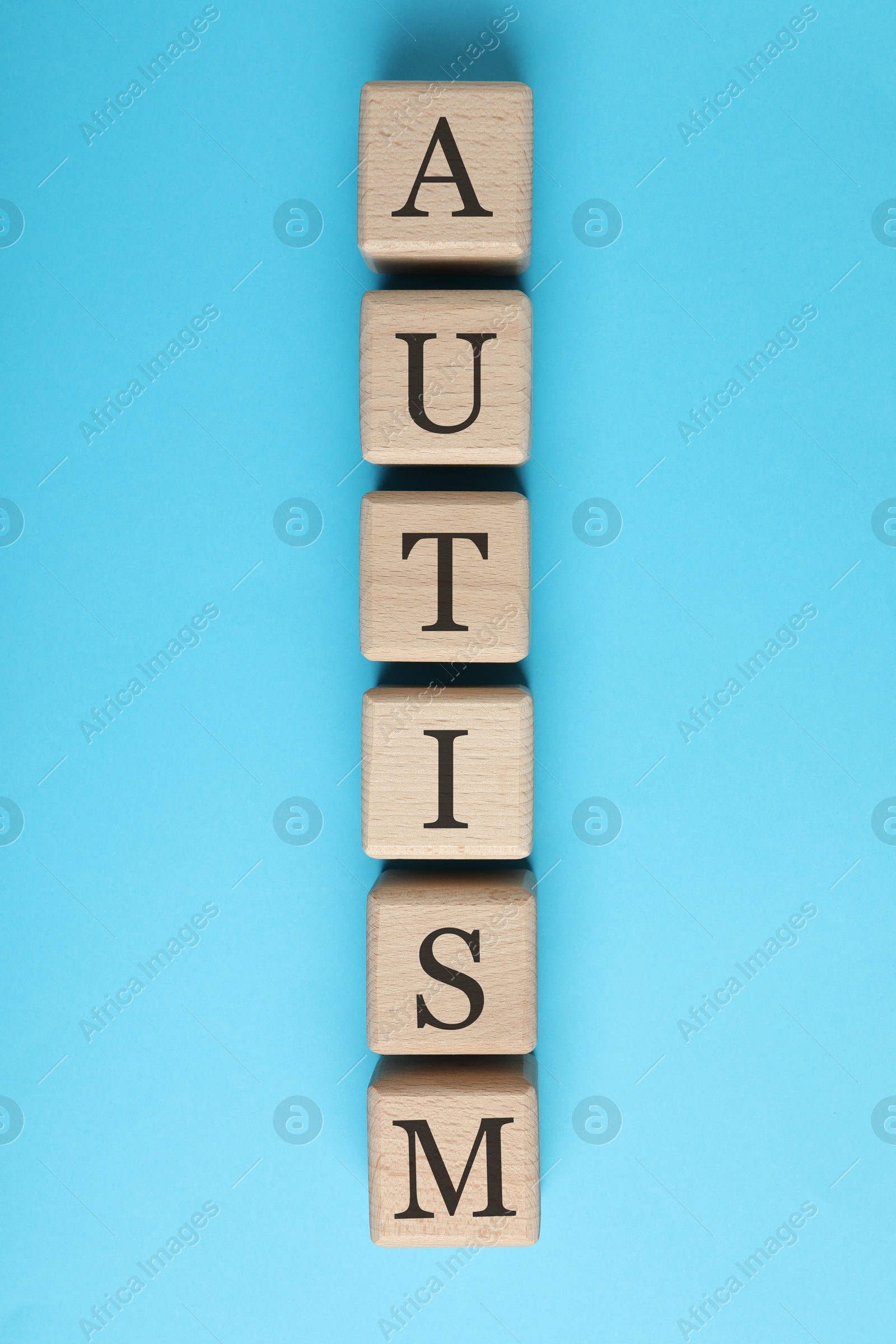 Photo of Word Autism made of wooden cubes on light blue background, top view