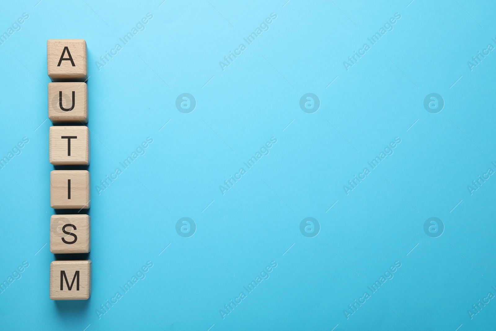 Photo of Word Autism made of wooden cubes on light blue background, top view. Space for text